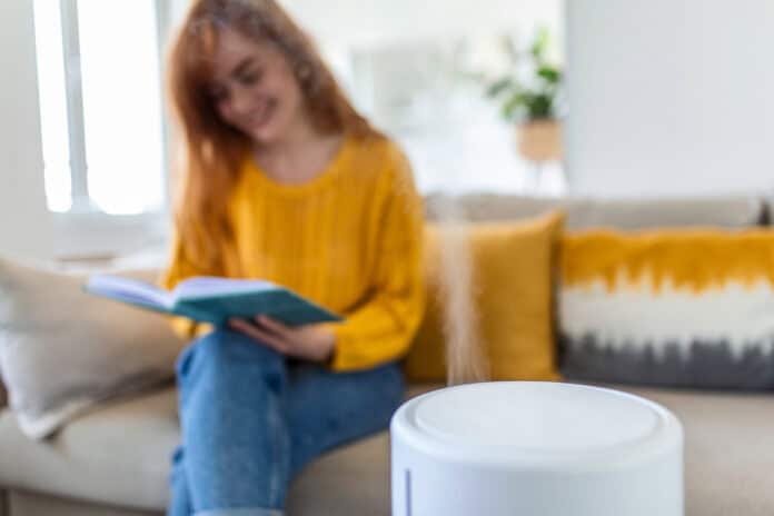 Modern air humidifier and blurred woman resting, reading a book on sofa on background luchtbevochtiger