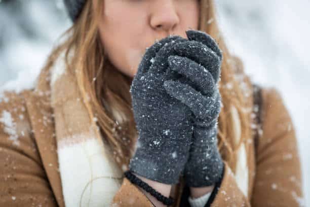 Young woman blowing arms to warm them because of the cold weather winterhanden